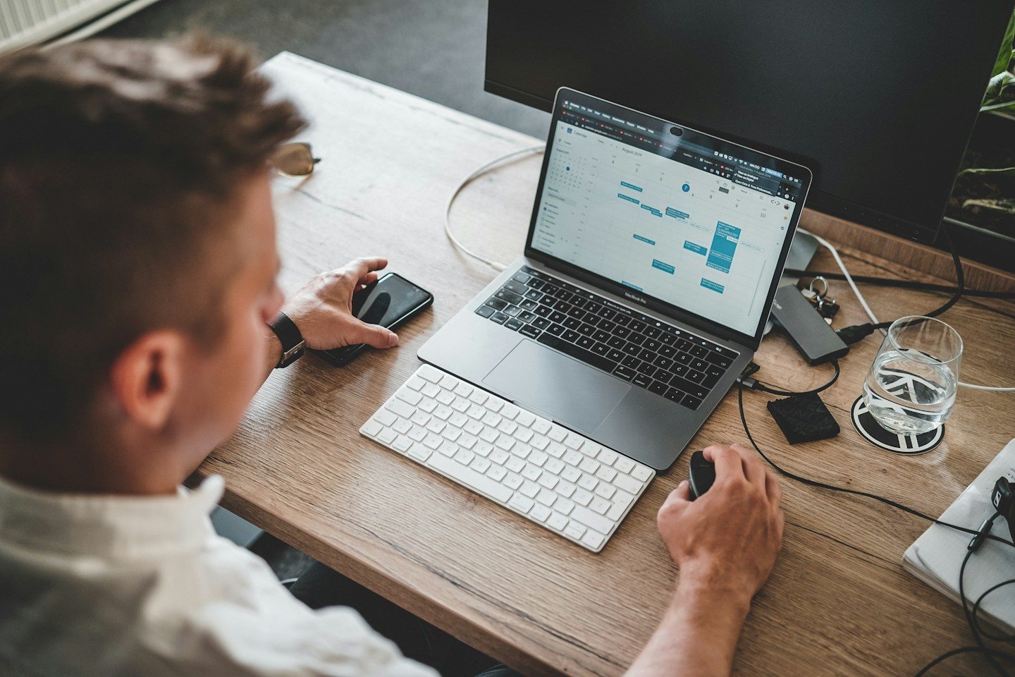 A person working at a laptop with a phone and external keyboard on the desk